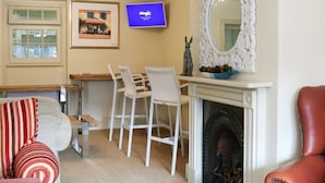 A living room with a fireplace, a television, a dining area with chairs, and a sofa with striped pillows. - The Quay B&B (Wells-next-the-Sea)