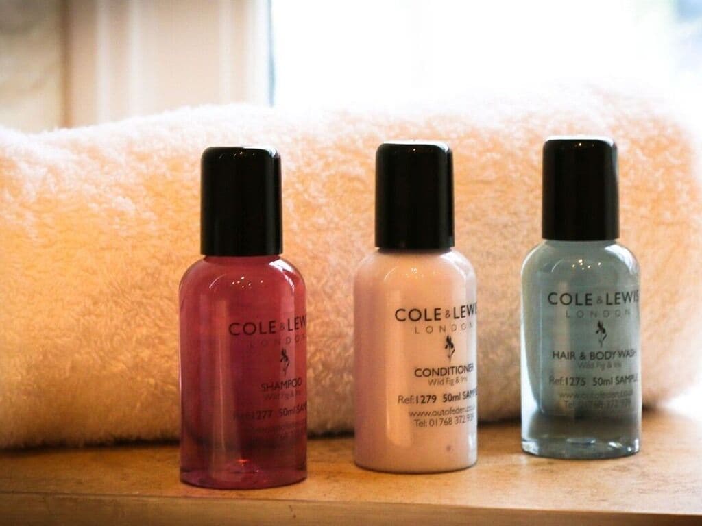 Three bottles of Cole & Lewy London hair and body wash on a wooden surface with a white towel in the background.