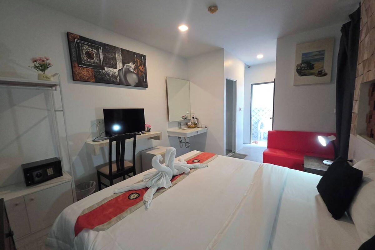 A hotel room with a bed, a television, a desk with a computer, a red chair, and a bathroom.