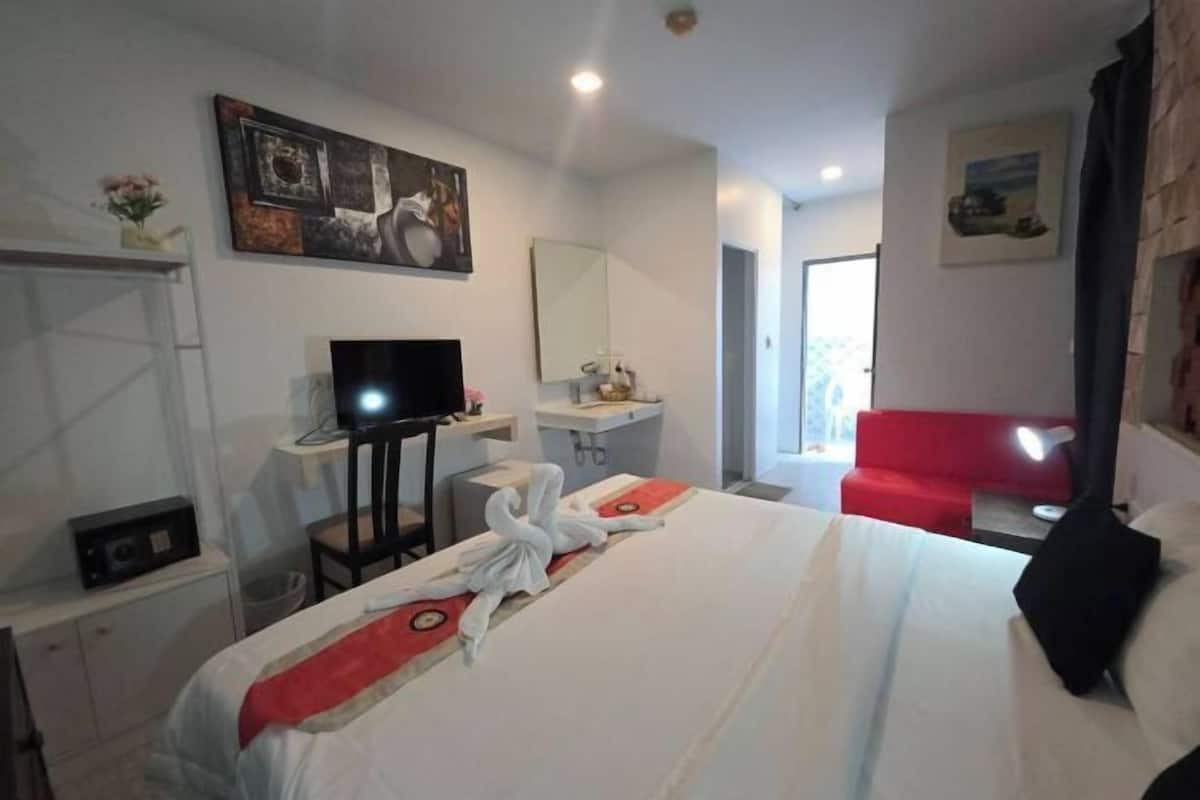 A hotel room with a bed, a television, a desk, a mirror, and a red couch.