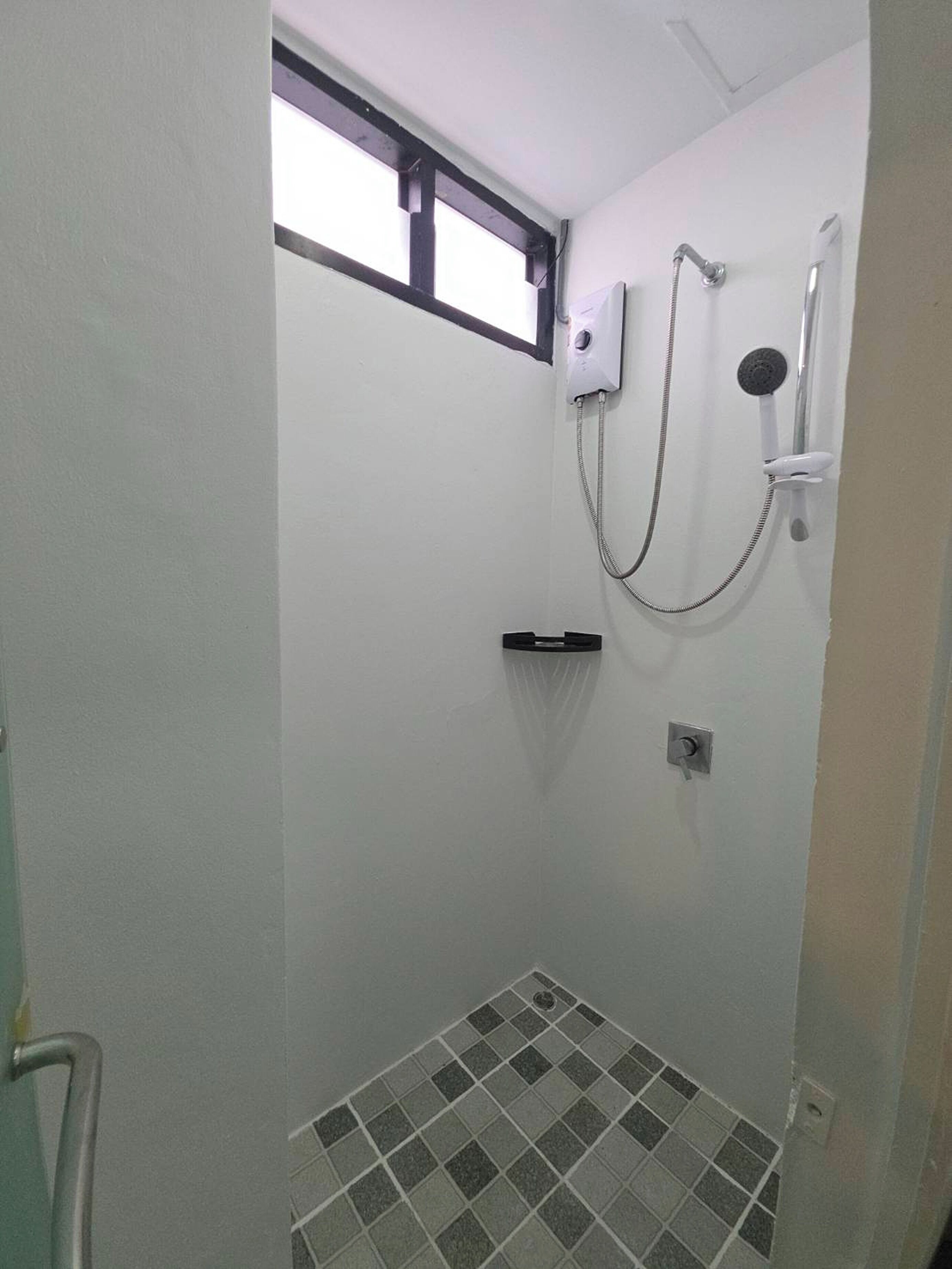 A small, tiled shower room with a window, a showerhead, and a control knob.
