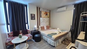 Una habitación de hotel con cama, sofá, mesita, silla, escritorio y aire acondicionado.