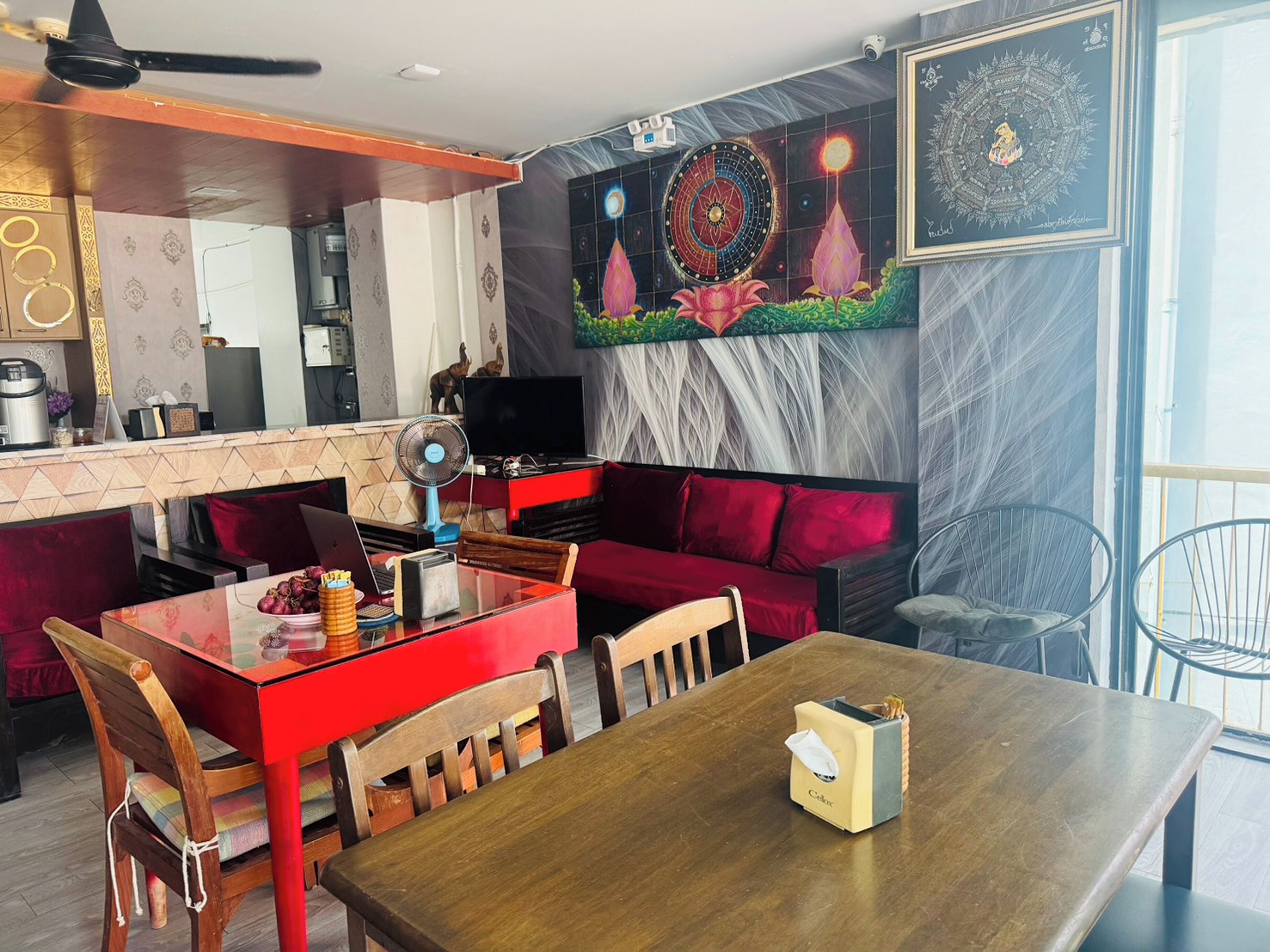 A modern kitchen with a red table, wooden chairs, a fan, and a TV.