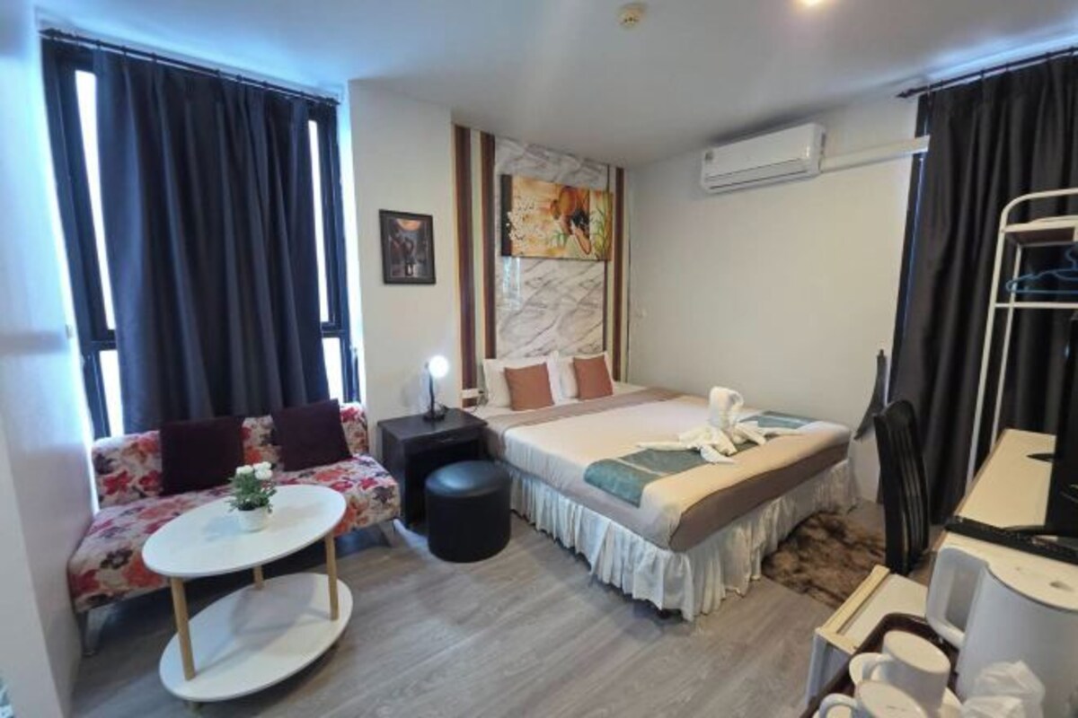 A hotel room with a bed, sofa, round table, and a small desk with a lamp.
