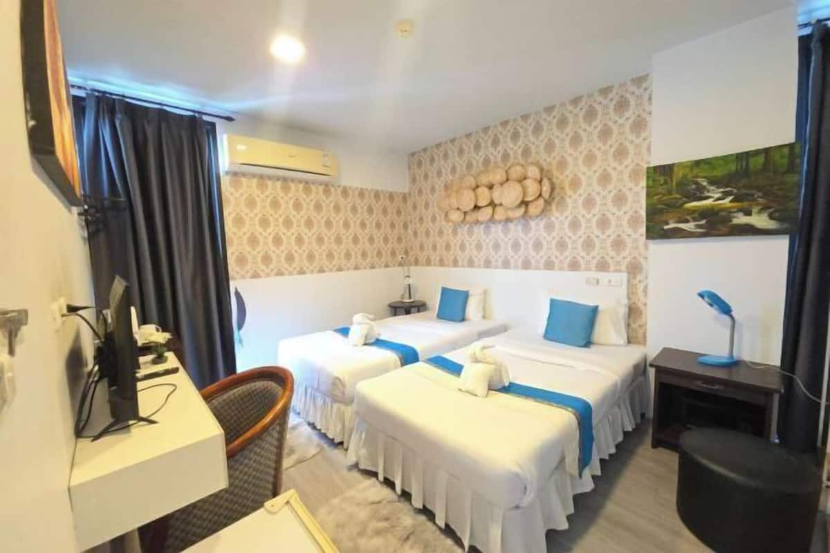 A hotel room with two beds, a desk, a chair, a TV, and a wall-mounted air conditioner.