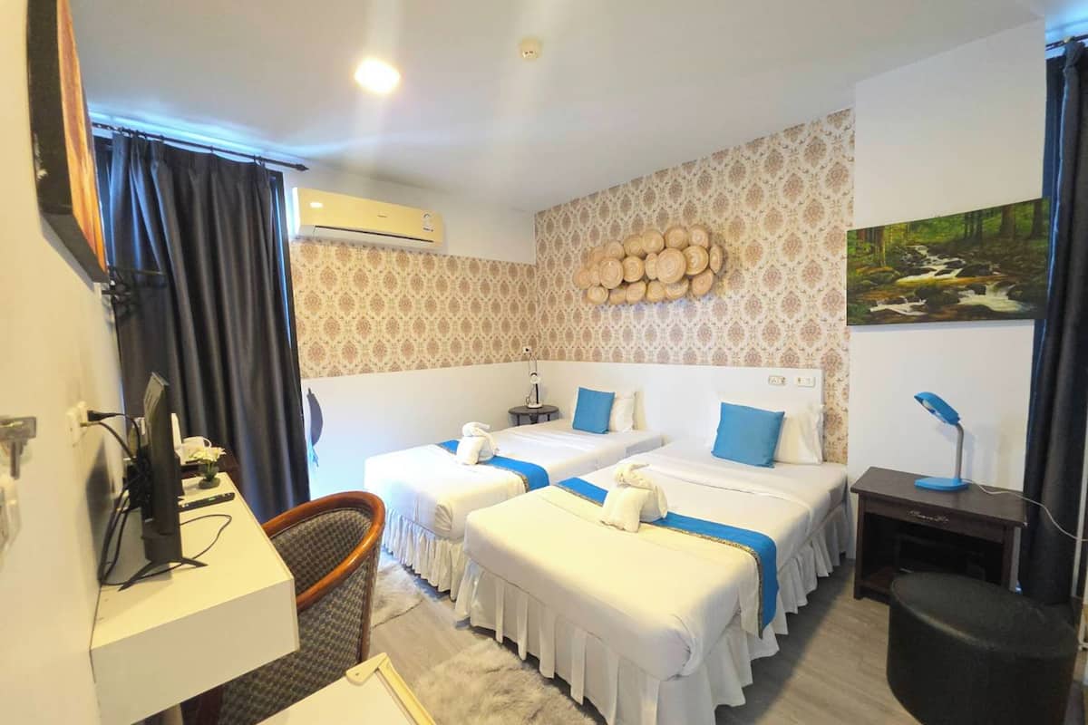 A hotel room with two beds, a desk, a chair, an air conditioner, and a painting on the wall.