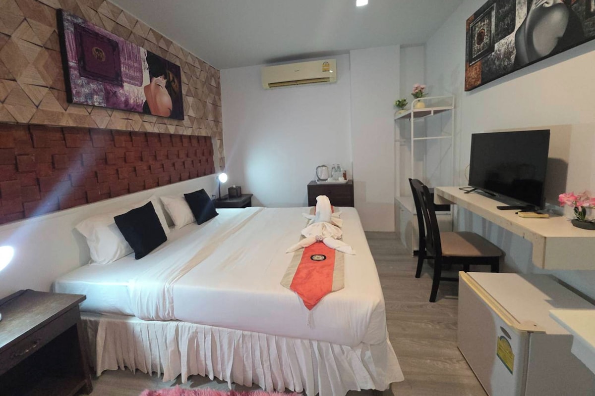 Een hotelkamer met een bed, een bureau met televisie, een stoel en een tafeltje met een lamp.