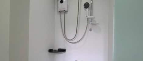 A small, enclosed shower area with a handheld showerhead, a wall-mounted faucet, and a control panel.