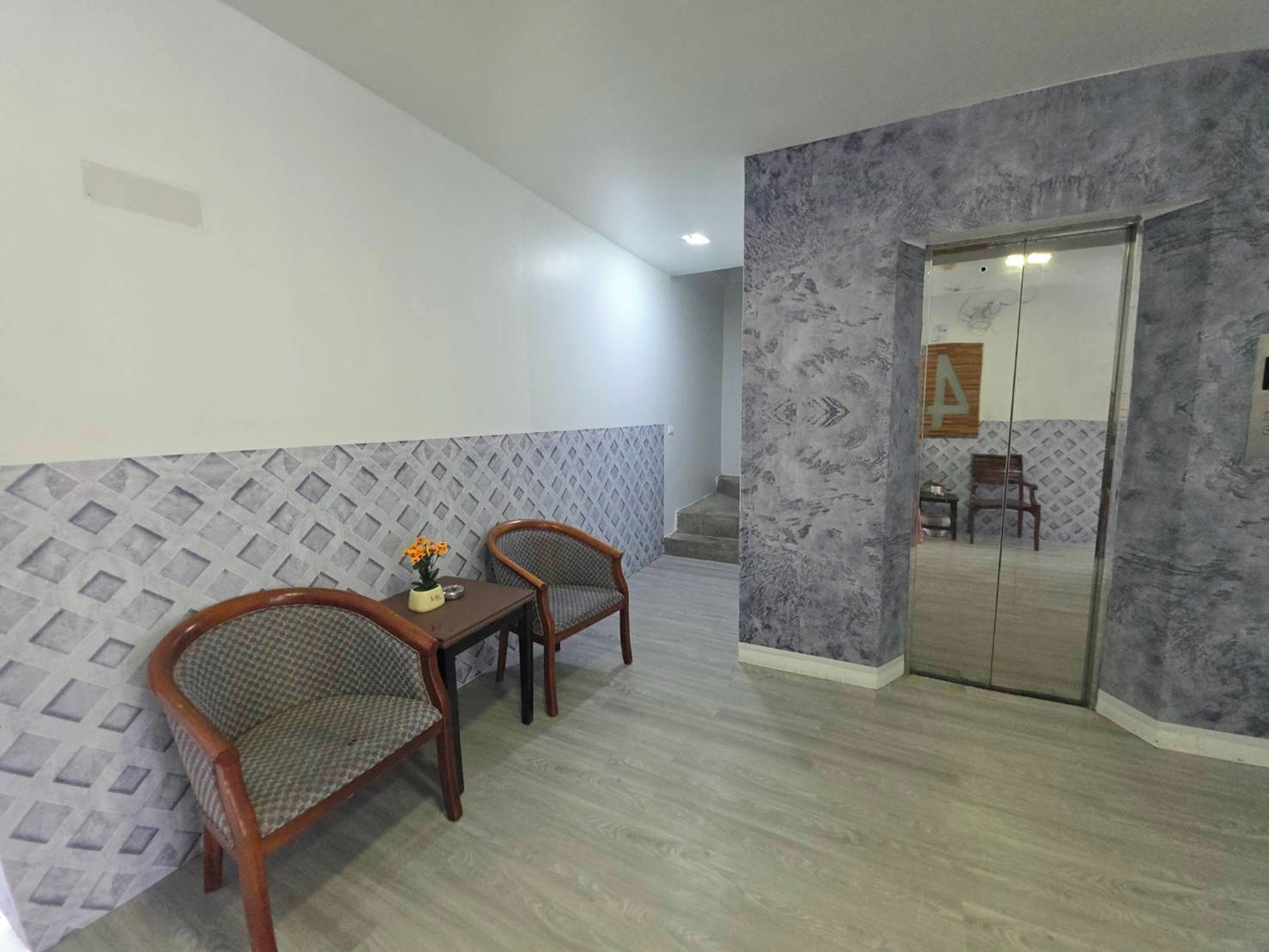 A hotel room with a dining area featuring two wooden chairs and a small table with a vase of flowers.