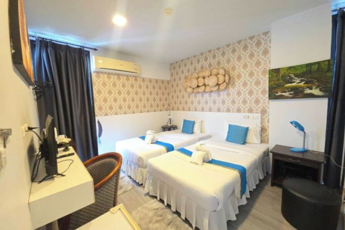 A hotel room with two beds, a desk, a chair, a TV, and a wall-mounted air conditioner.