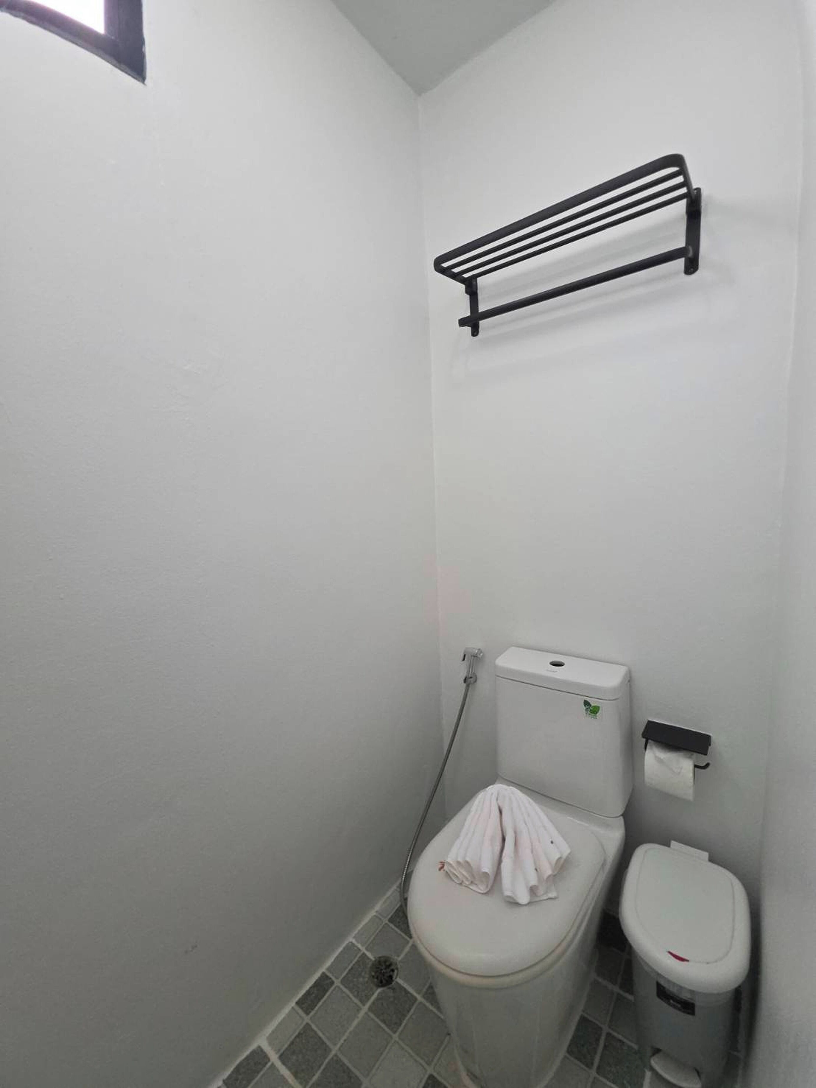 Une petite salle de bain blanche, équipée de toilettes, d’une poubelle et d’un porte-serviettes.