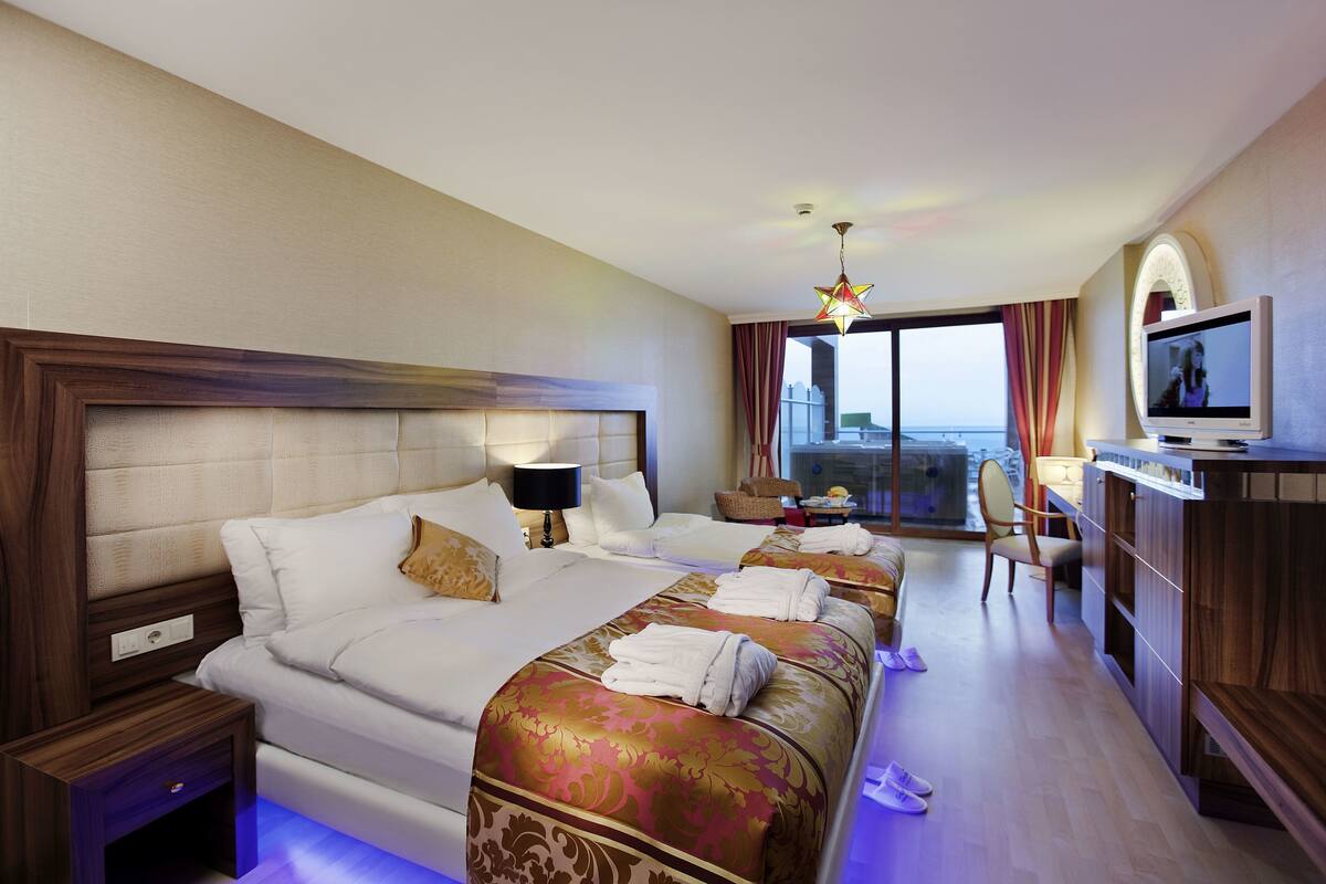 A hotel room with two beds, a television, a desk, and a balcony with a view.