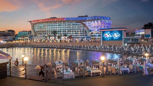 A waterfront hotel with a curved facade, multiple balconies, and a pool area with dining tables and chairs. - Granada Luxury Resort Okurcalar - All Inclusive (Alanya)