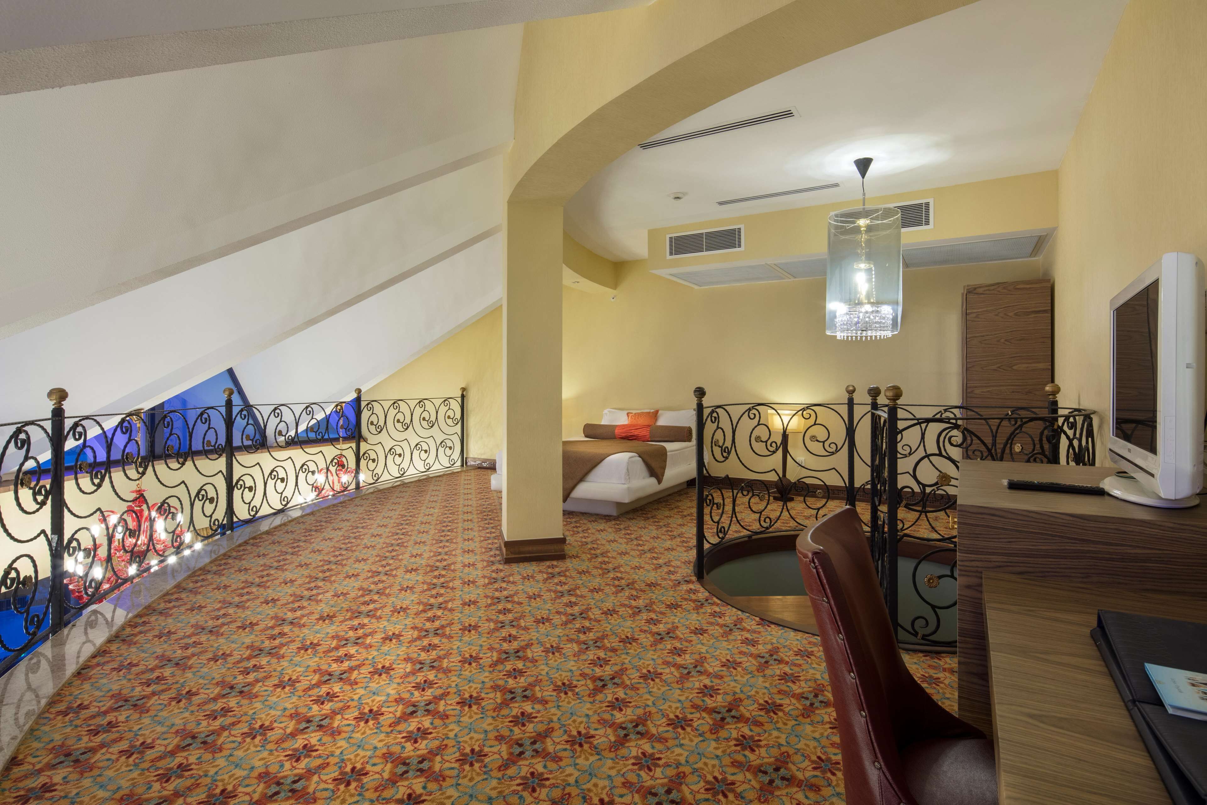 Hotelkamer met een kamerbreed tapijt, een bed met kussen, een bureau met computer en een balkon met hekwerk.