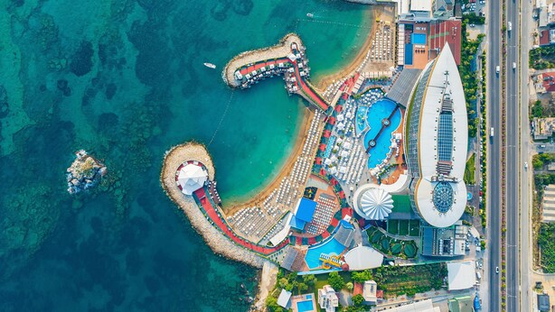 An aerial view of a resort with a large pool, a winding water slide, and a beach area with umbrellas. - Granada Luxury Resort Okurcalar - All Inclusive (Alanya)