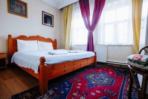 A bedroom with a wooden bed, a red and blue patterned rug, a chair, and a window with curtains. - Kose Pension (Nevsehir)