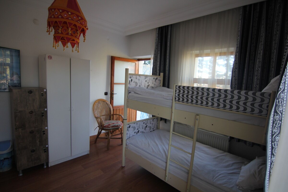 A bunk bed room with a wooden wardrobe, a chair, and a hanging lamp.