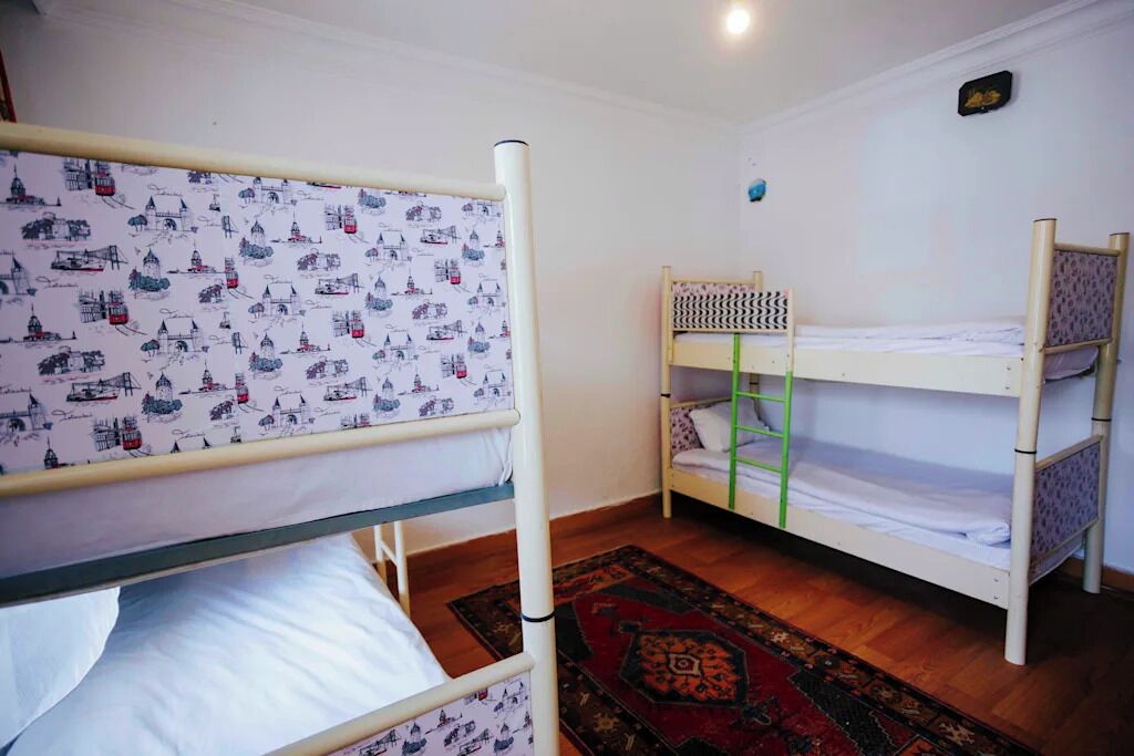A room with bunk beds, a patterned curtain, a wooden floor, and a small rug.
