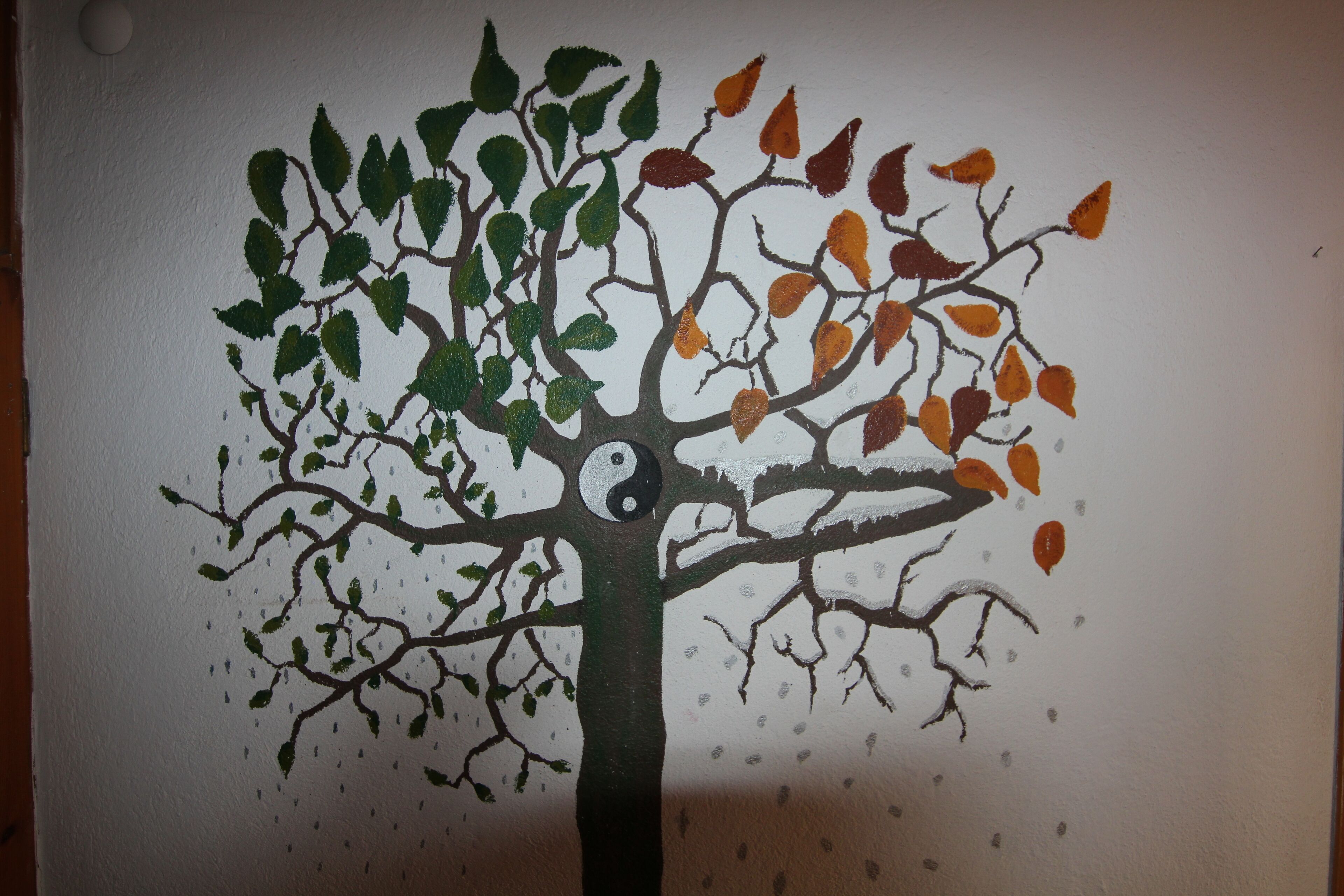 A tree with green and orange leaves against a plain wall.
