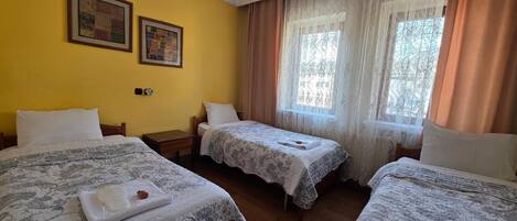 Habitación de hotel con tres camas, piso de madera, pared amarilla y dos cuadros enmarcados.