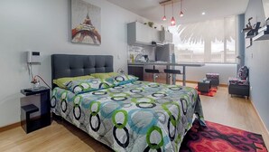 A modern bedroom with a bed, a desk, and a kitchenette. - Las Palmas Apartment 306 (Bogotá)