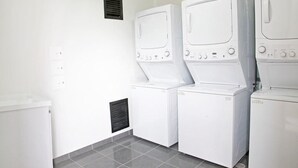 A laundry room with three stacked washers and dryers, a vent on the wall, and a trash bin. - Las Palmas Apartment 306 (Bogotá)