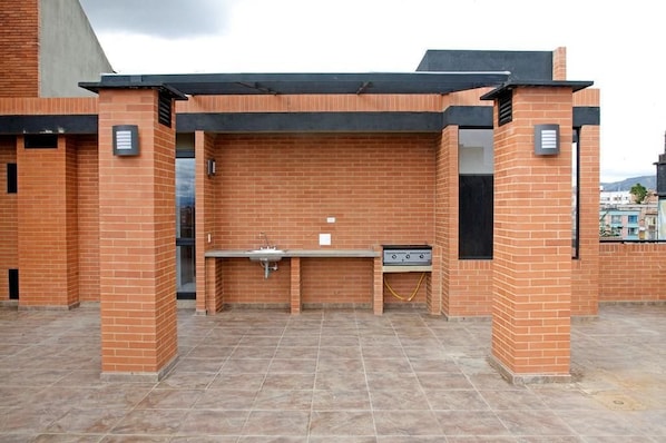 An outdoor brick barbecue area with a sink and grill, surrounded by a tiled floor.