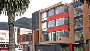 A modern building with a red and black facade, large windows, and a palm tree in the foreground. - Las Palmas Apartment 306 (Bogotá)