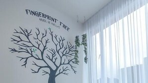 Une pièce dont un mur est décoré d’un motif représentant un arbre, avec une petite table sur laquelle est posé un vase, et deux chaises.