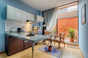 A compact kitchen with a central island, a dining area with chairs, and a view of a brick wall and plants through a sliding door.