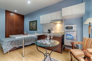 A compact living space with a kitchenette, a dining area with a glass table, a sofa, and a microwave.