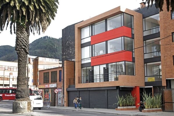 A modern building with a red and black facade, large windows, and a palm tree in the foreground.