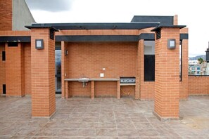 An outdoor brick barbecue area with a sink and grill, surrounded by a tiled floor.