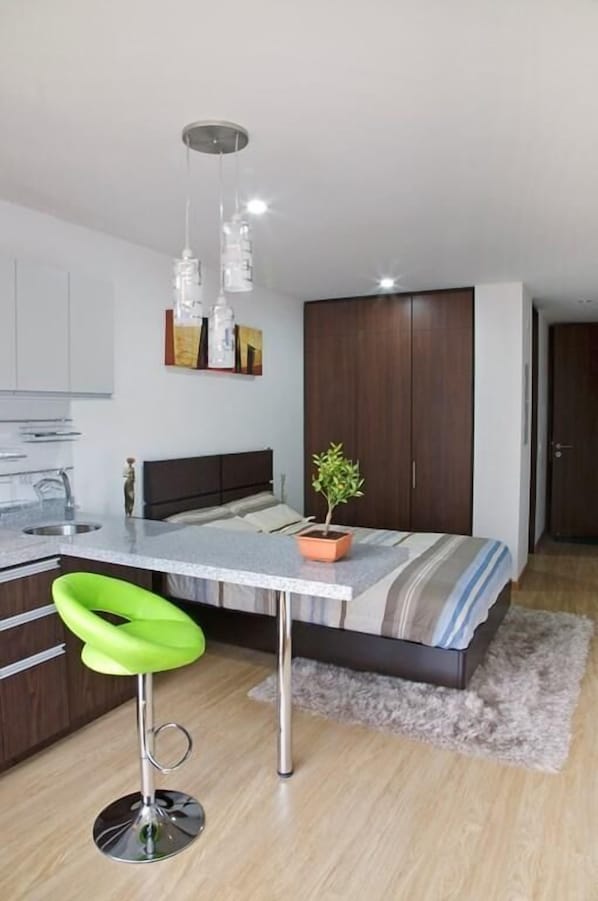 A compact bedroom with a bed, bedside table, and a small stool.