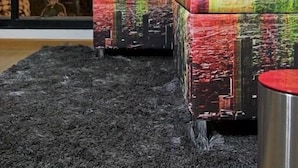 Un intérieur moderne avec une grande fenêtre, un tapis noir à texture marquée et des poufs colorés à motifs.