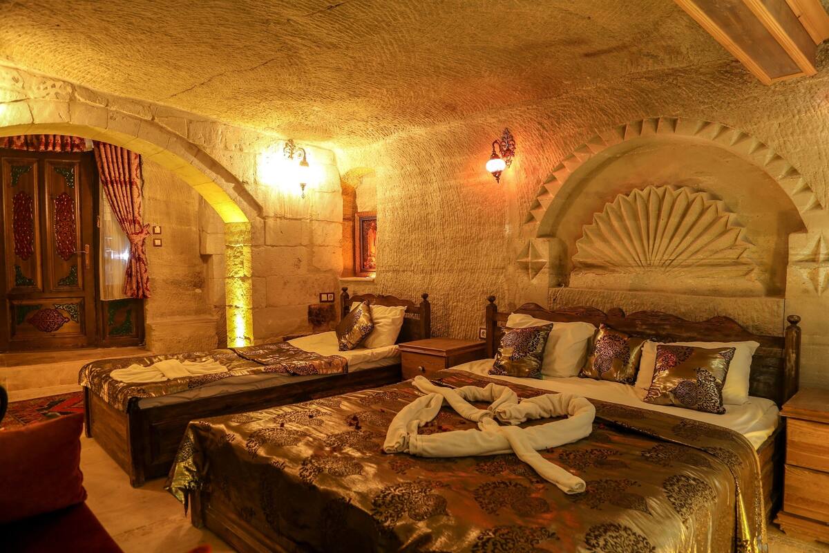 Quarto tradicional com duas camas, paredes de pedra e um arco decorativo.