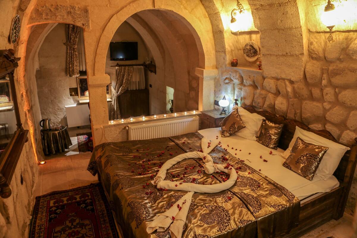 Quarto com parede de pedra, cama com colcha estampada, espelho e um candelabro.