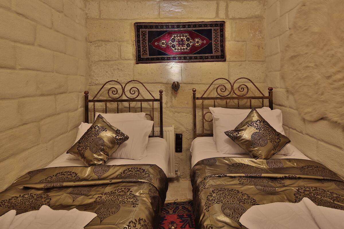 Quarto com duas camas, cada uma adornada com roupa de cama e almofadas detalhadas, um painel decorativo na parede e um radiador.