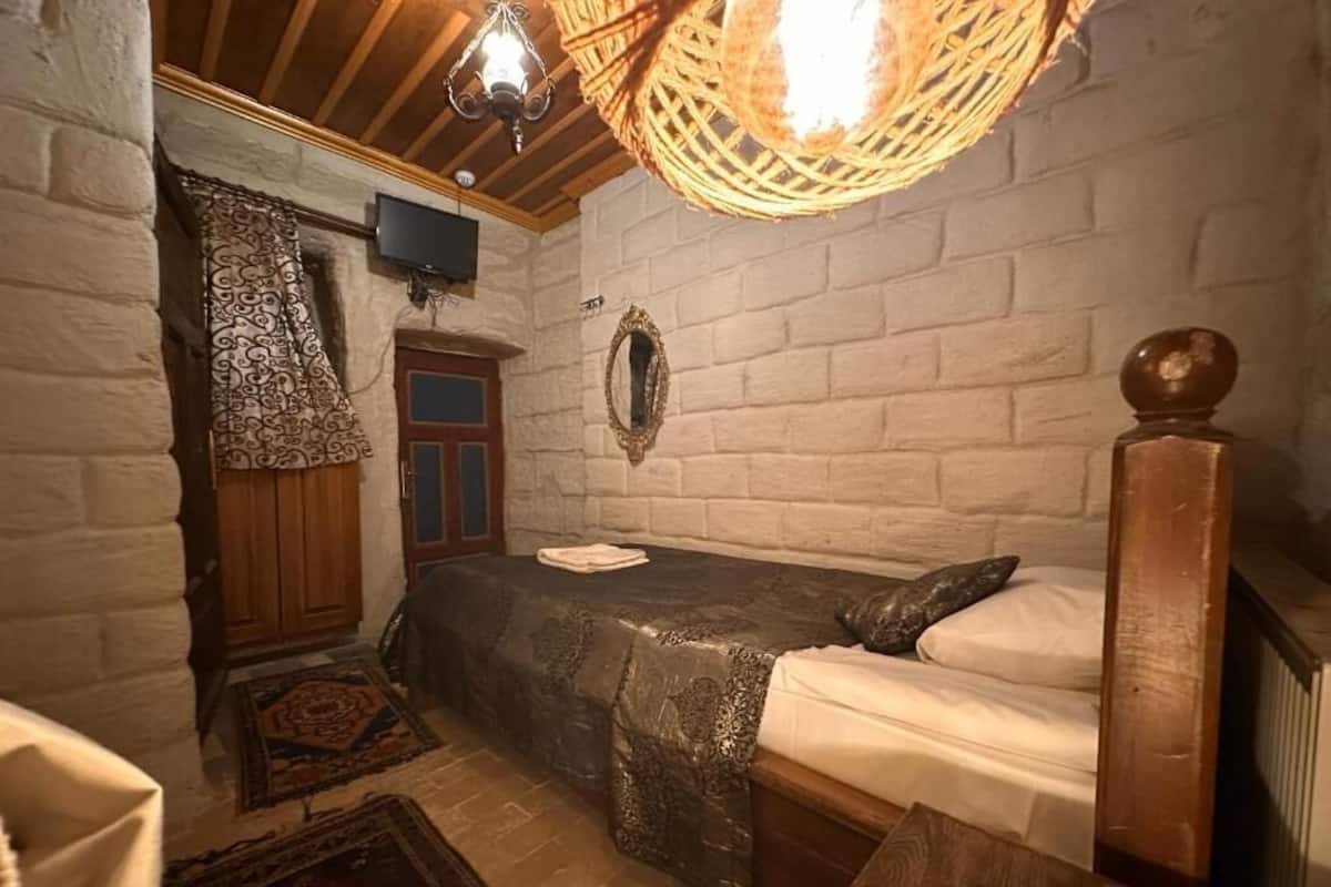 Quarto com cama, cadeira de madeira, televisão, espelho e cortina estampada.
