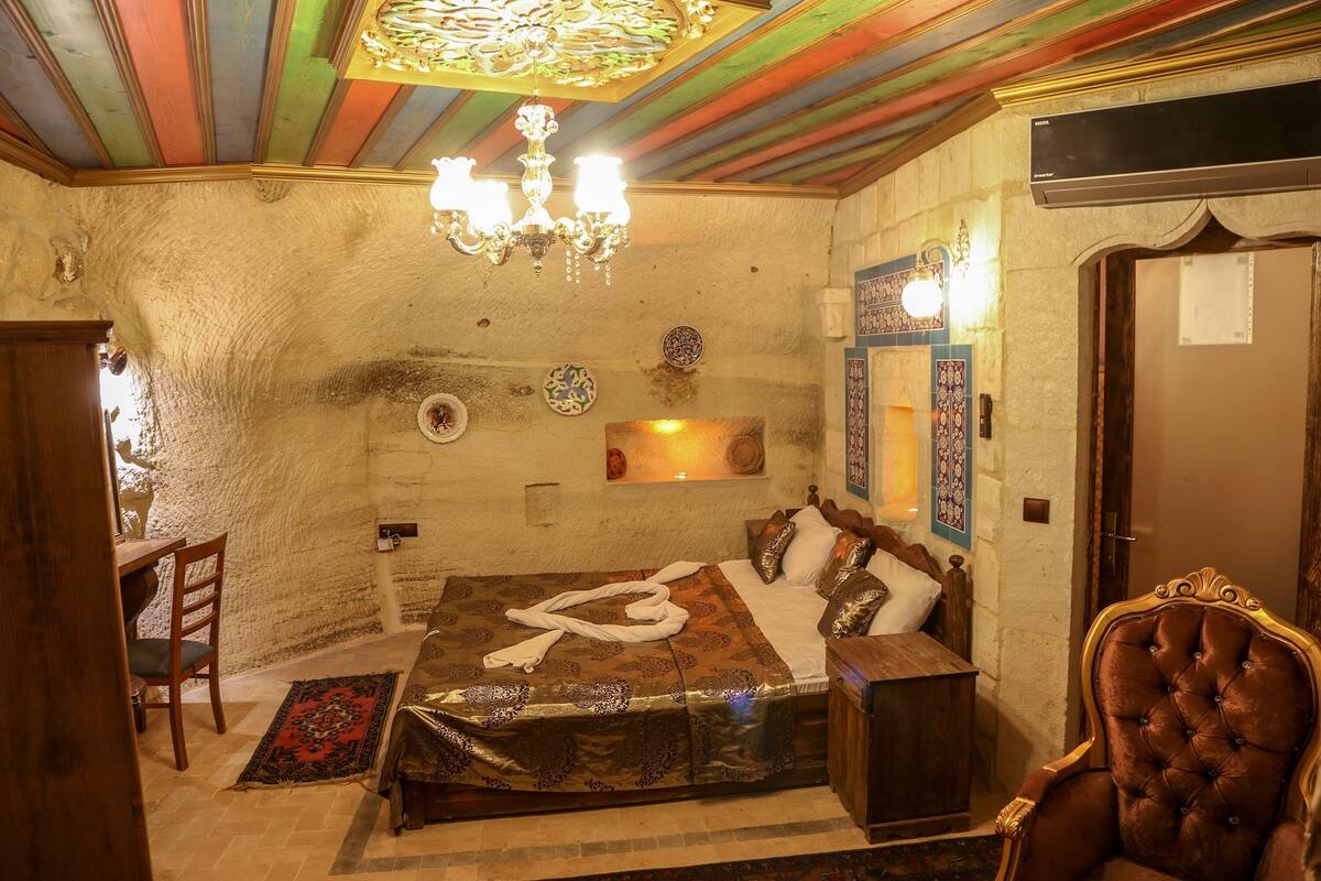 Um quarto com uma cama, um candelabro, uma cadeira de madeira e um ar condicionado fixado na parede.