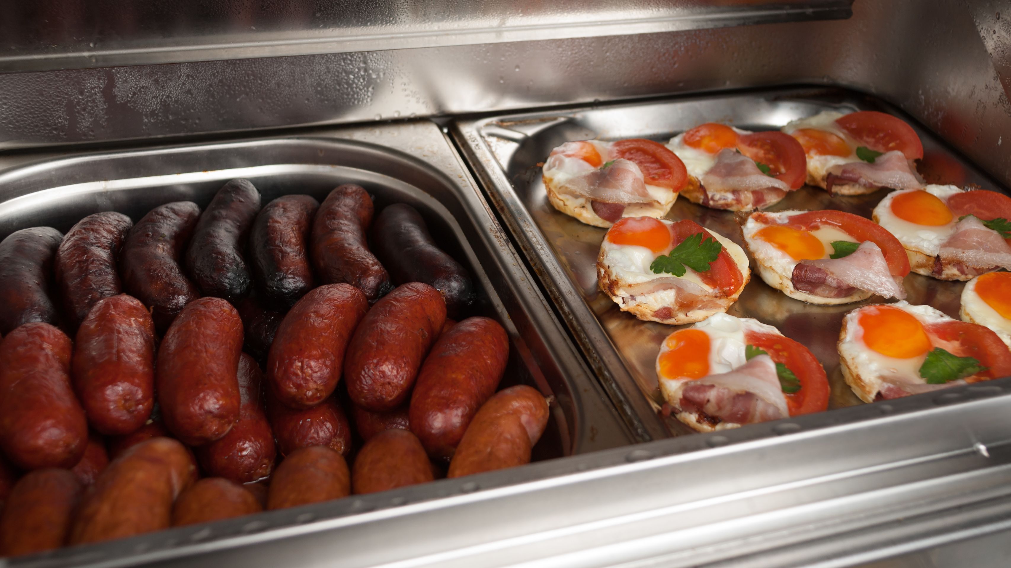 Een ontbijtbuffet met diverse gerechten, waaronder worstjes en eieren met bacon en tomaten.