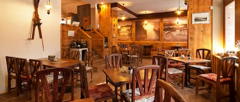 A restaurant with wooden interiors, multiple tables and chairs, and a staircase leading to an upper level.