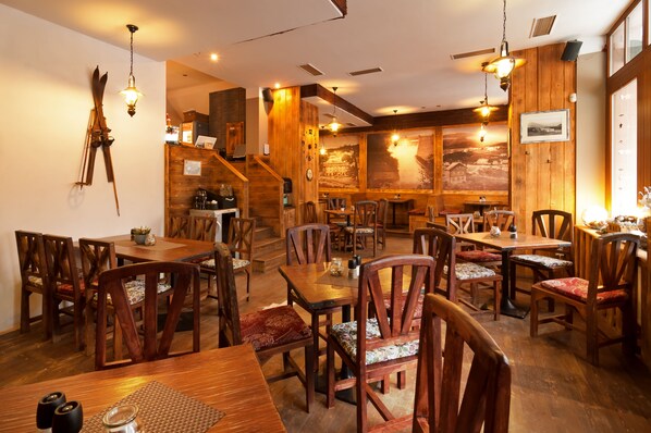 Un restaurante con interiores de madera, varias mesas y sillas, y una escalera que sube a un nivel superior.