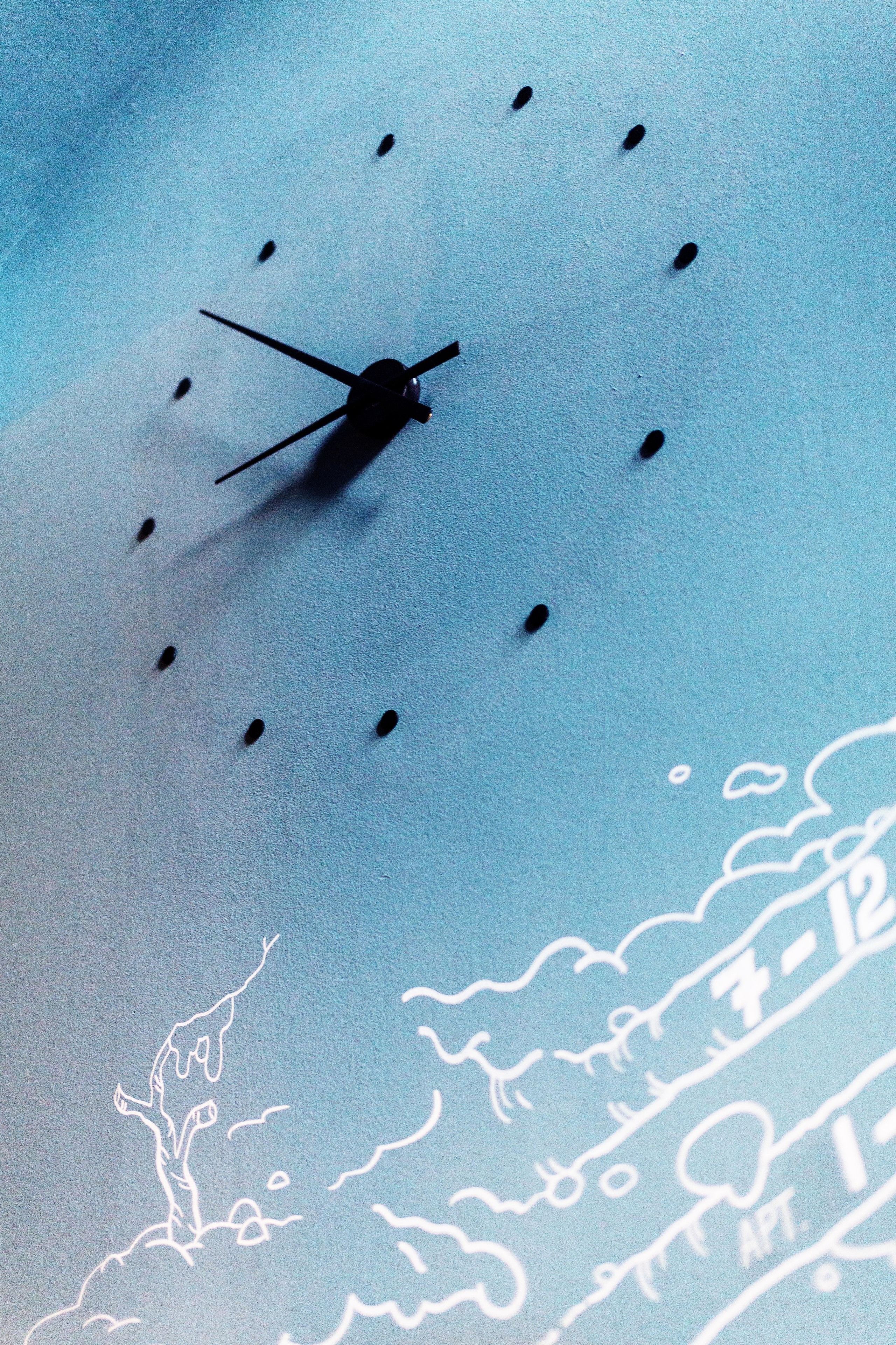 A wall clock with a minimalist design, featuring a silhouette of a bird and a tree.