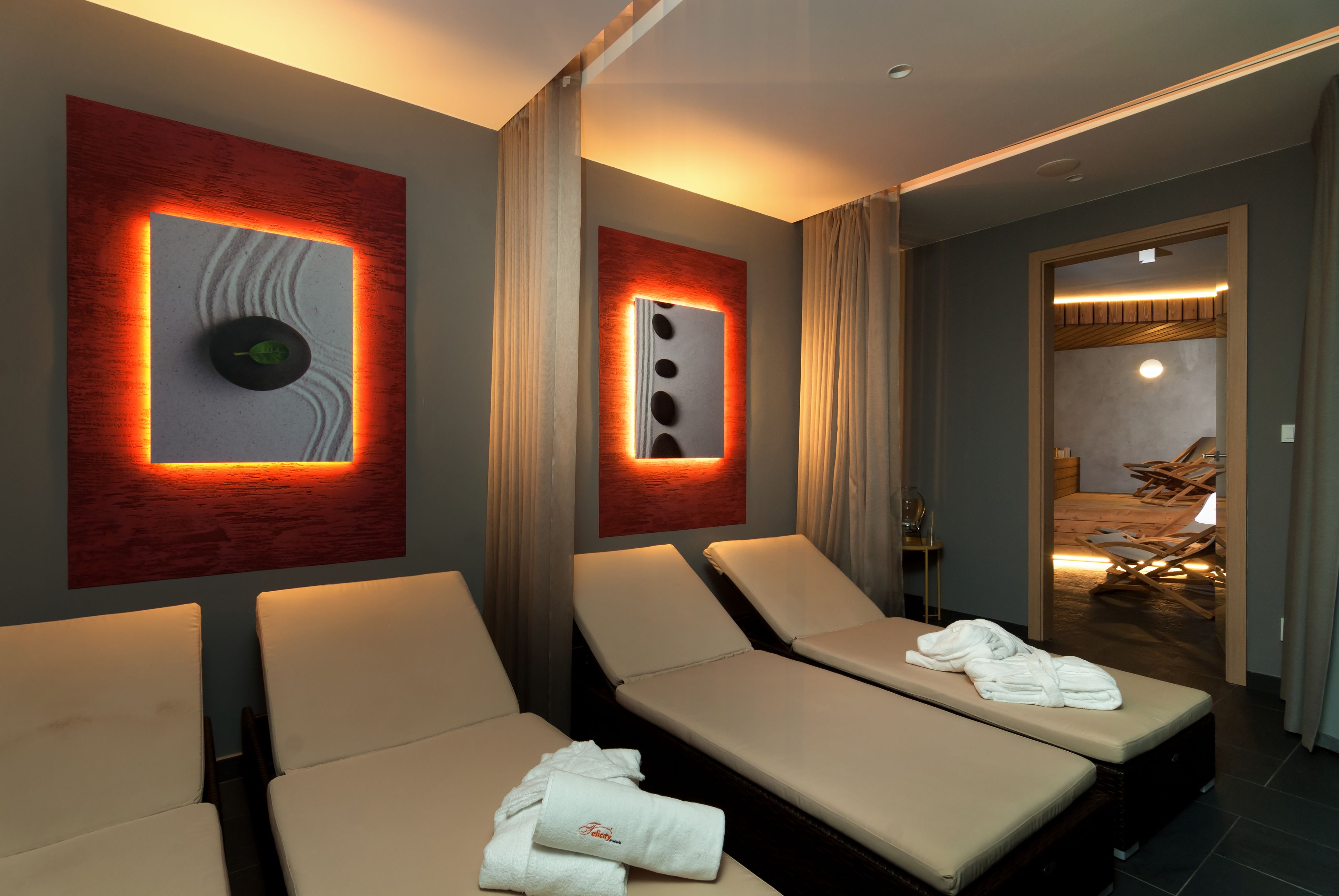 Ein Hotelzimmer mit zwei Liegesesseln, einem Massagesessel und einem an der Wand befestigten Massagetisch.