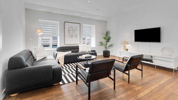 A modern living room with a sofa, coffee table, and chairs, a flat-screen TV, and a potted plant. - The SFX Old Port (Montreal)