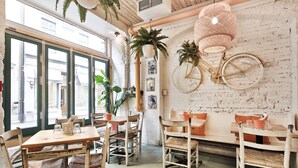 A rustic cafe interior with wooden tables and chairs, potted plants, and a vintage bicycle mounted on the wall. - The SFX Old Port (Montreal)