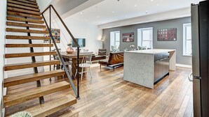 A modern kitchen with a wooden staircase, a dining area, and a kitchen island. - The SFX Old Port (Montreal)