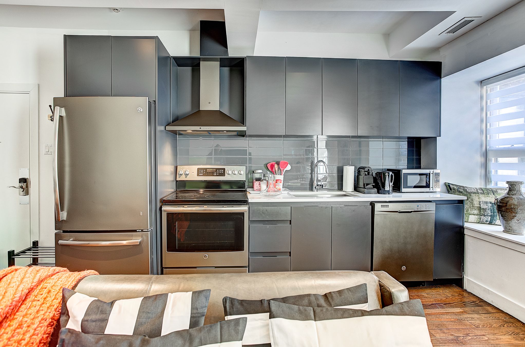 A modern kitchen with stainless steel appliances, grey cabinets, and a built-in oven.
