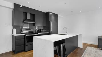 Une cuisine moderne avec des meubles de couleur sombre, des appareils en acier inoxydable, un îlot central doté de tabourets et un plancher en bois.